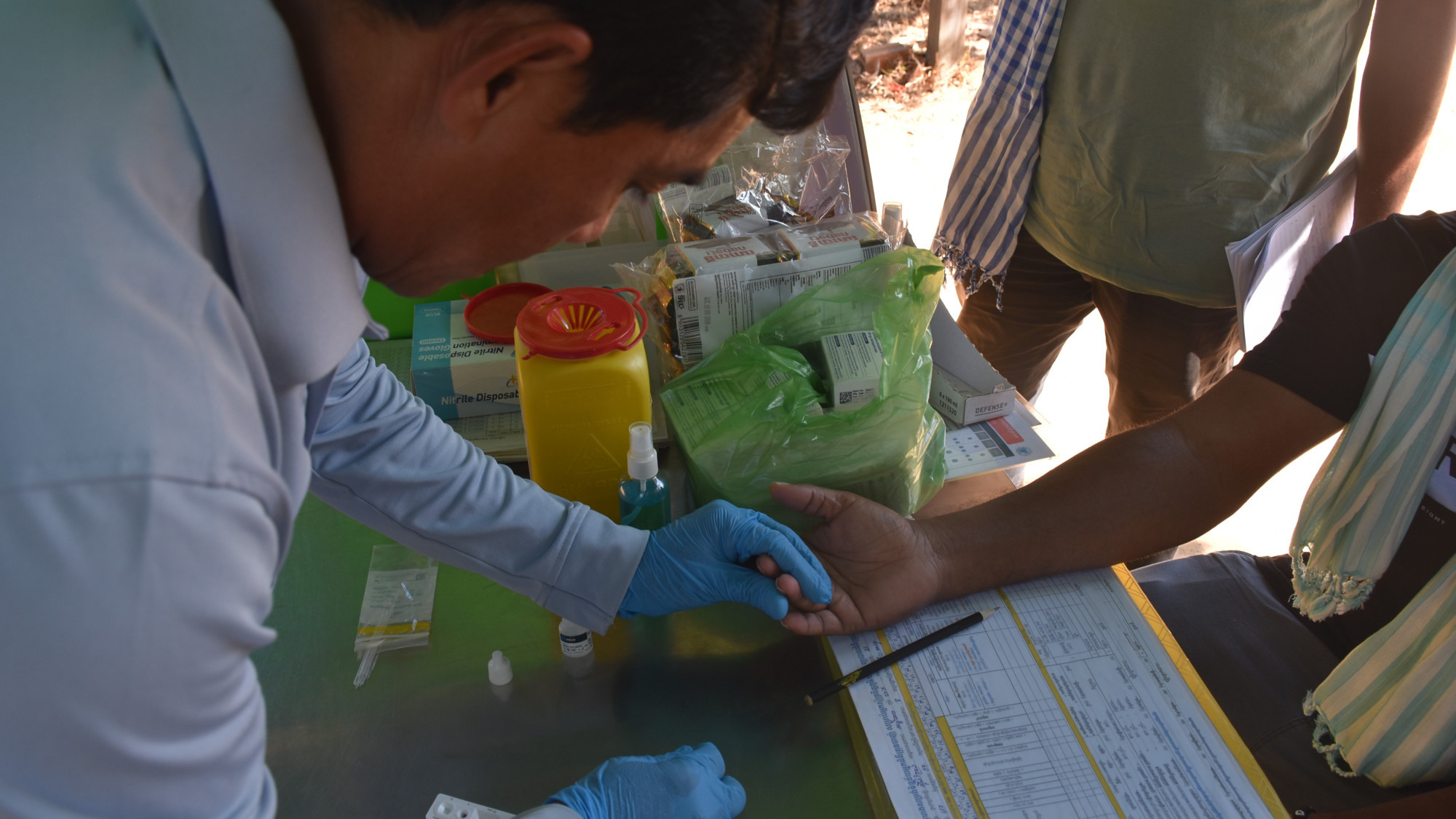 A Mobile Malaria Worker performing a malaria rapid diagnostic test (RDT) and collecting a finger-prick blood sample from a visitor during field surveillance activities in Stung Treng Province.