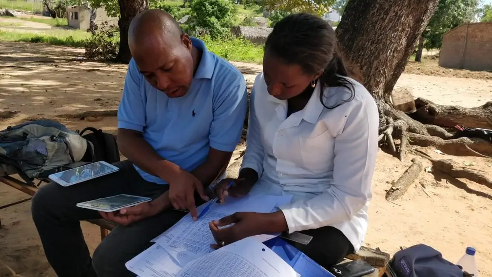 Mozambique upSCALE Malaria Consortium technician and CHW cross-checking data books with upSCALE app