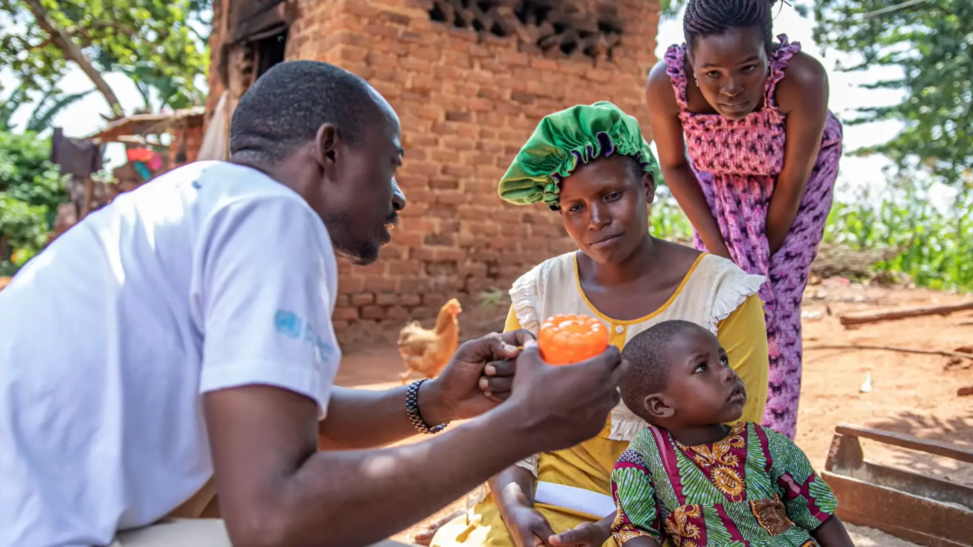 Health worker shows a Mossie-GO spatial repellent device to a mother and her two children, Uganda