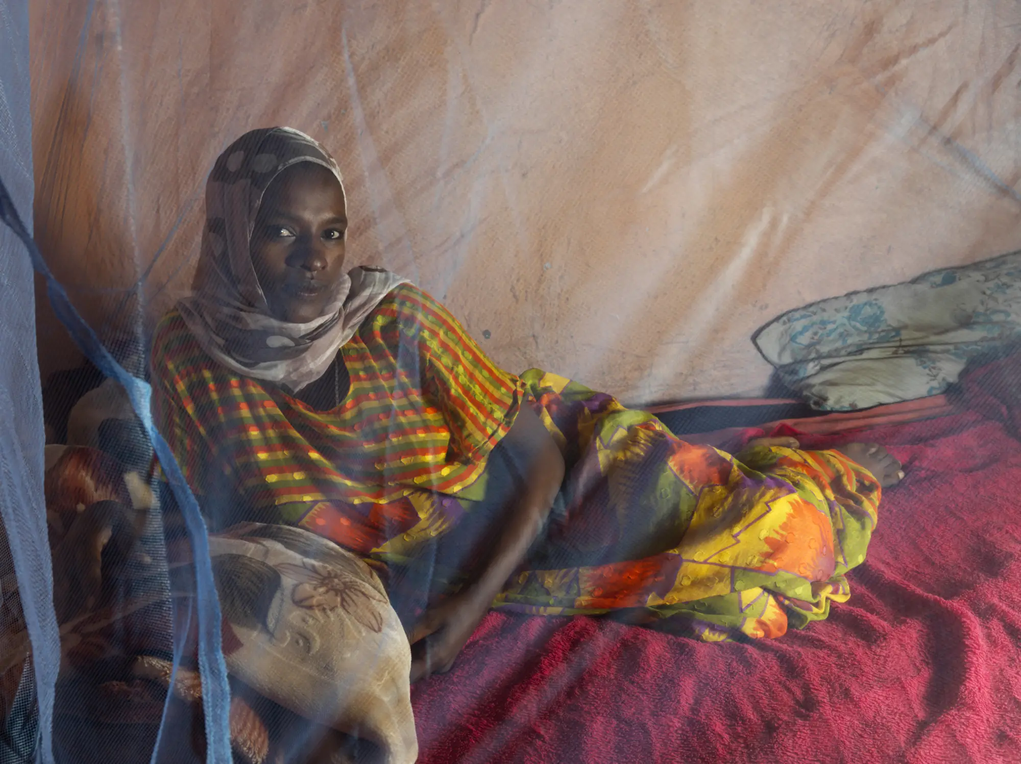 A woman sits behind an insecticide-treated net, as part of the Transform project in Ethiopia