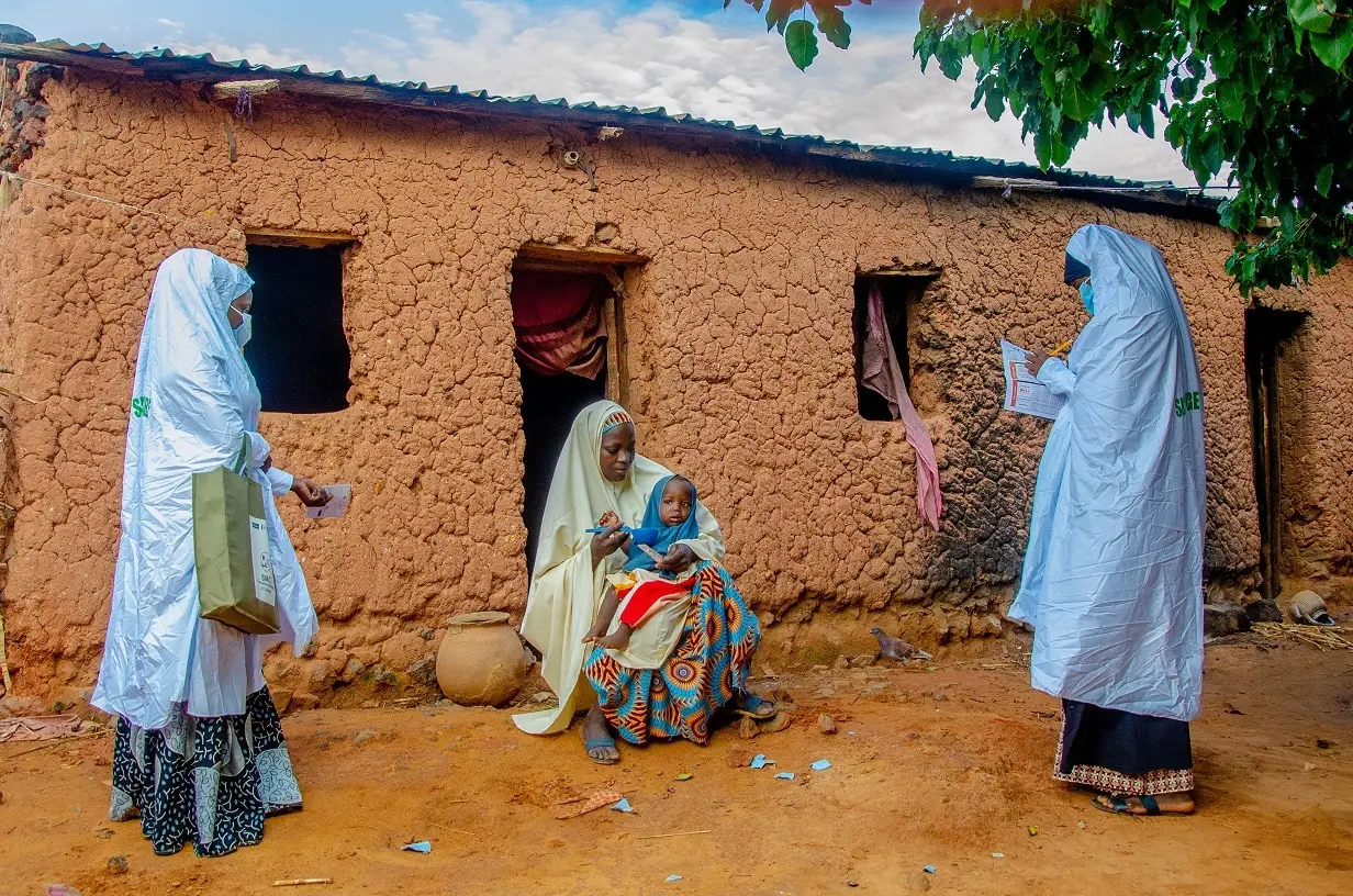 Two healthcare workers talk to a woman with her child in Nigeria, 2020