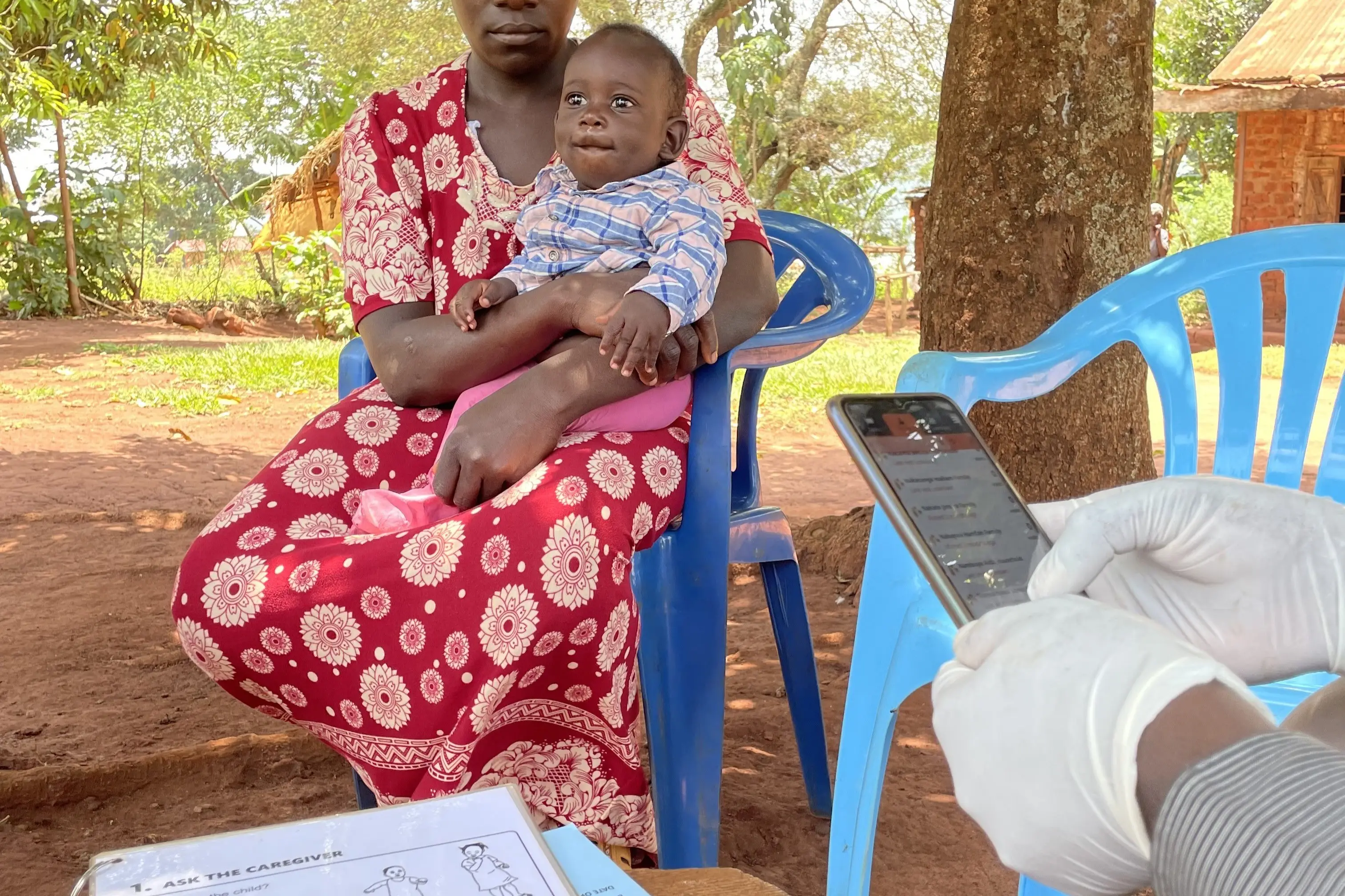 A healthcare worker fills out details on their smartphone of a woman with her child at a SMC and PReS workshop in Uganda