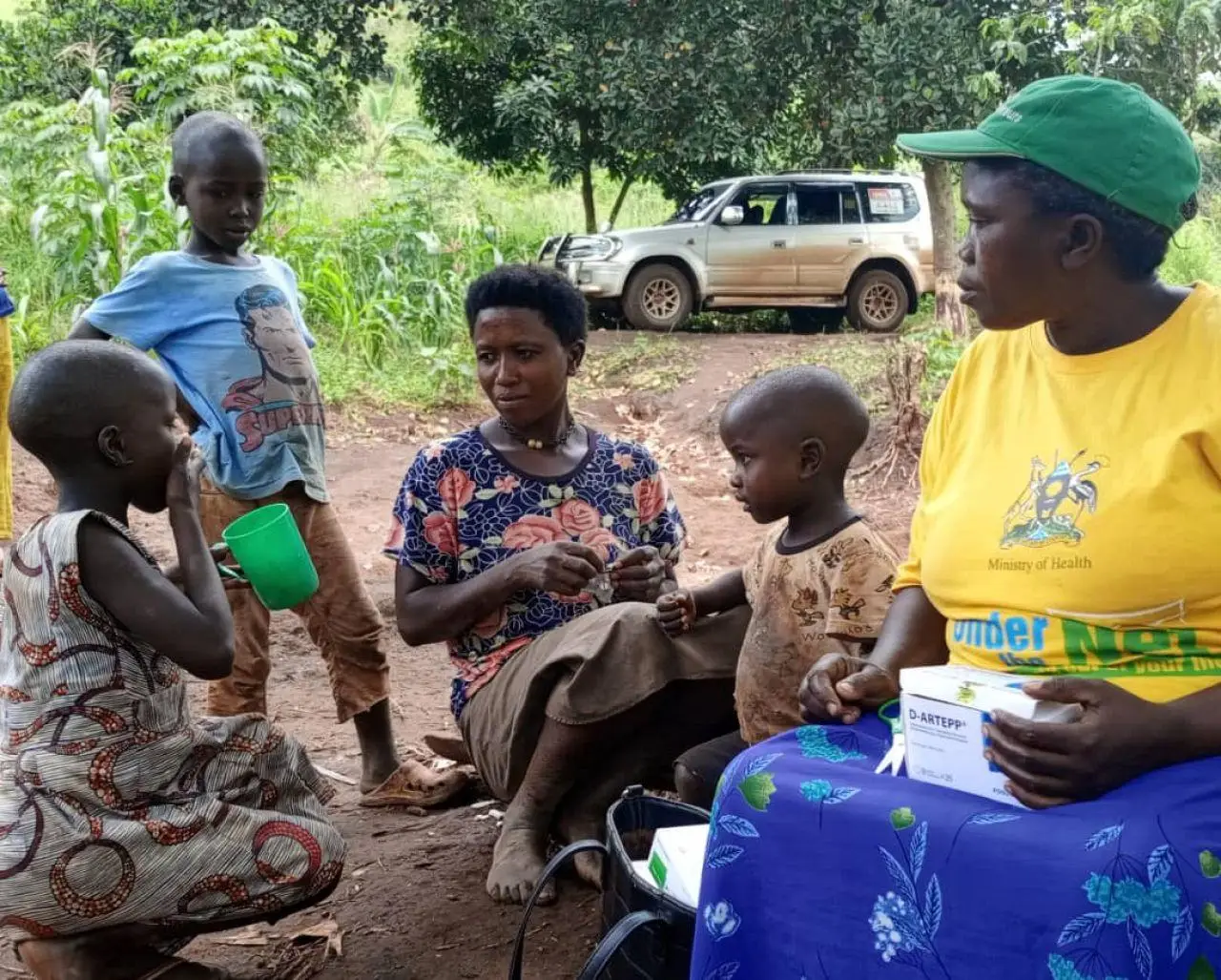 A village health team member observes a caregiver administering dihydroartemisinin-piperaquine as part of mass drug administration, Mubende district, Uganda