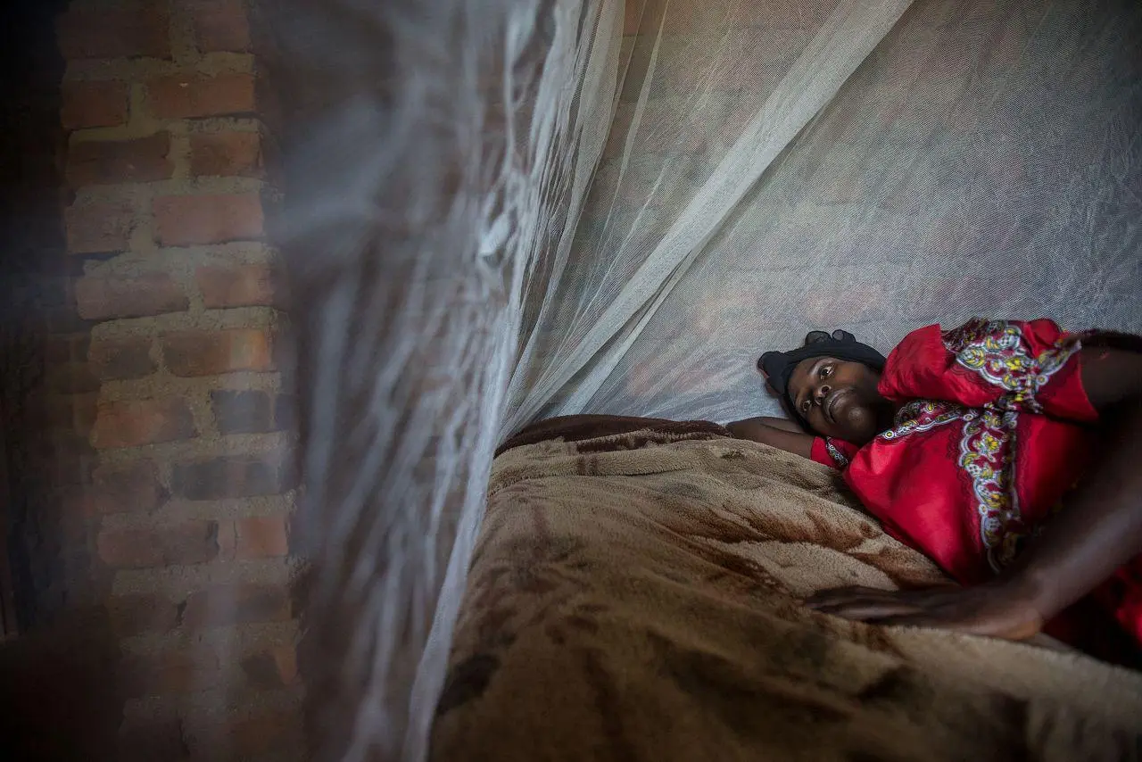 Najjuko, an expectant mother of six months, lies inside her insecticide-treated net in an attempt to prevent mosquito bites, Uganda