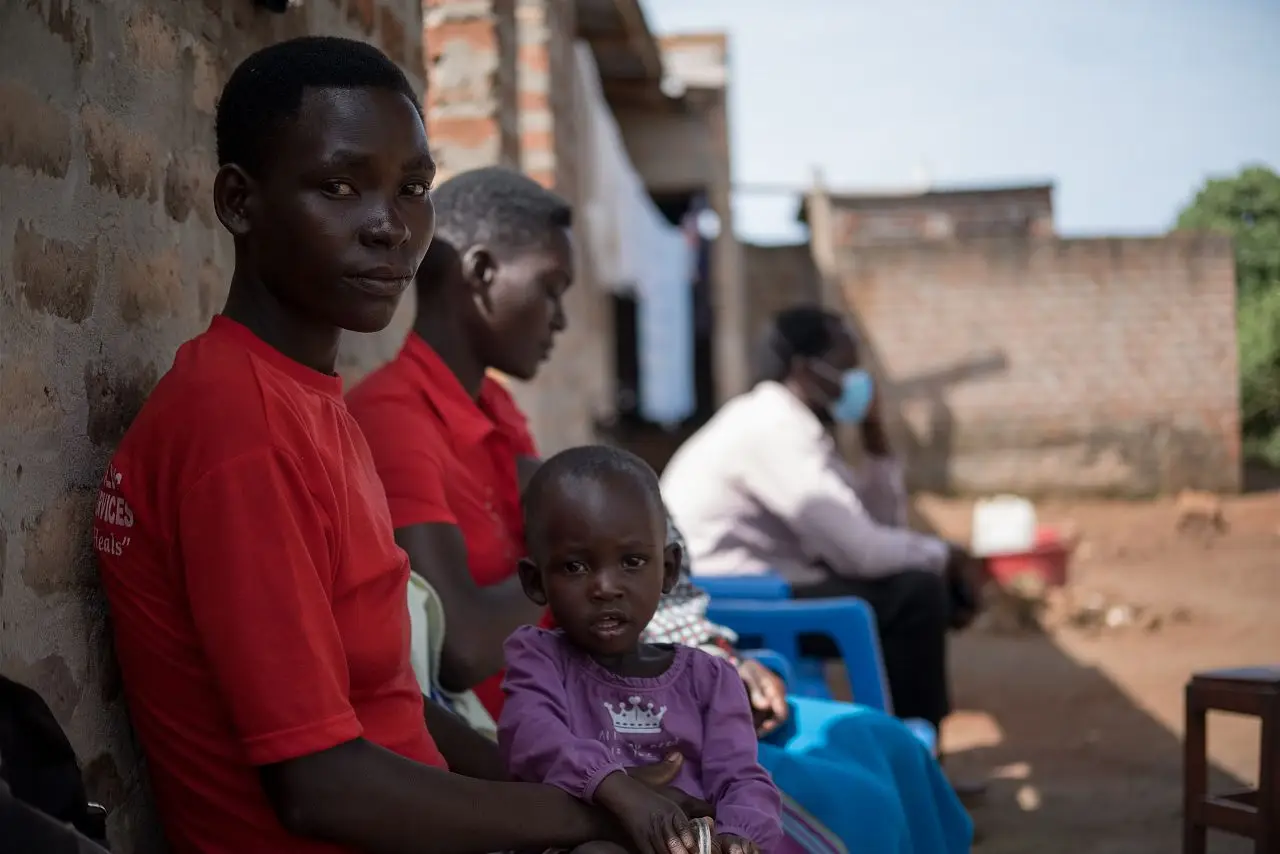 Akullu and her daughter wait in line for an appointment with a village health team, Kole district, Uganda