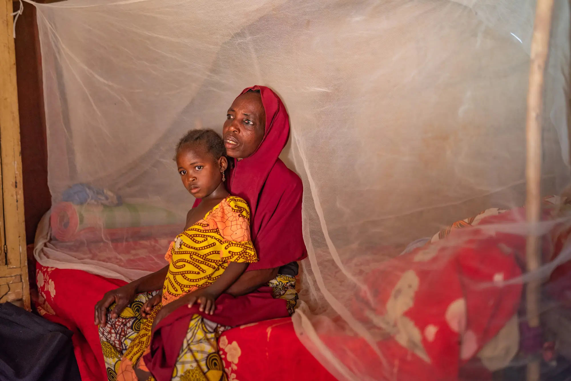 A child sitting on a woman's lap under a mosquito net in Jigawa, Nigeria in 2023