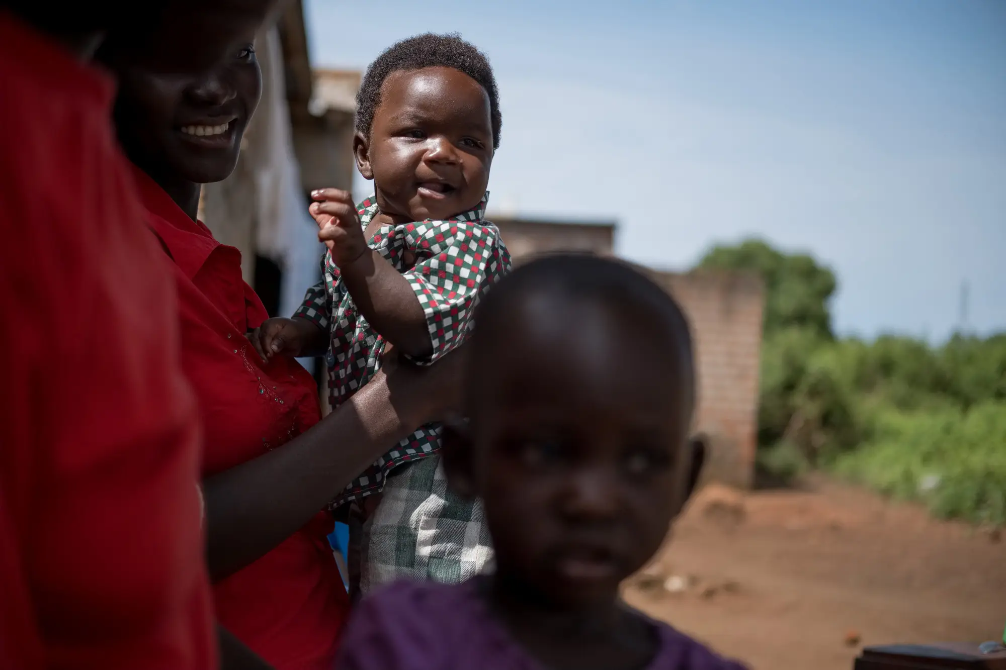 A woman holding a child and another child standing in front of the camera in Uganda, 2022