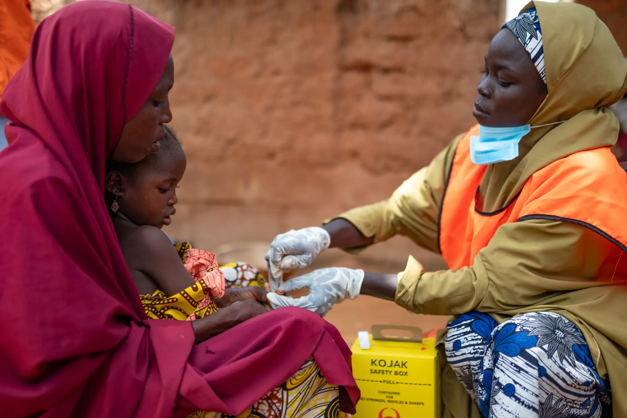 A healthcare worker helps a child in a woman's lap in Jigawa, Nigeria in 2023