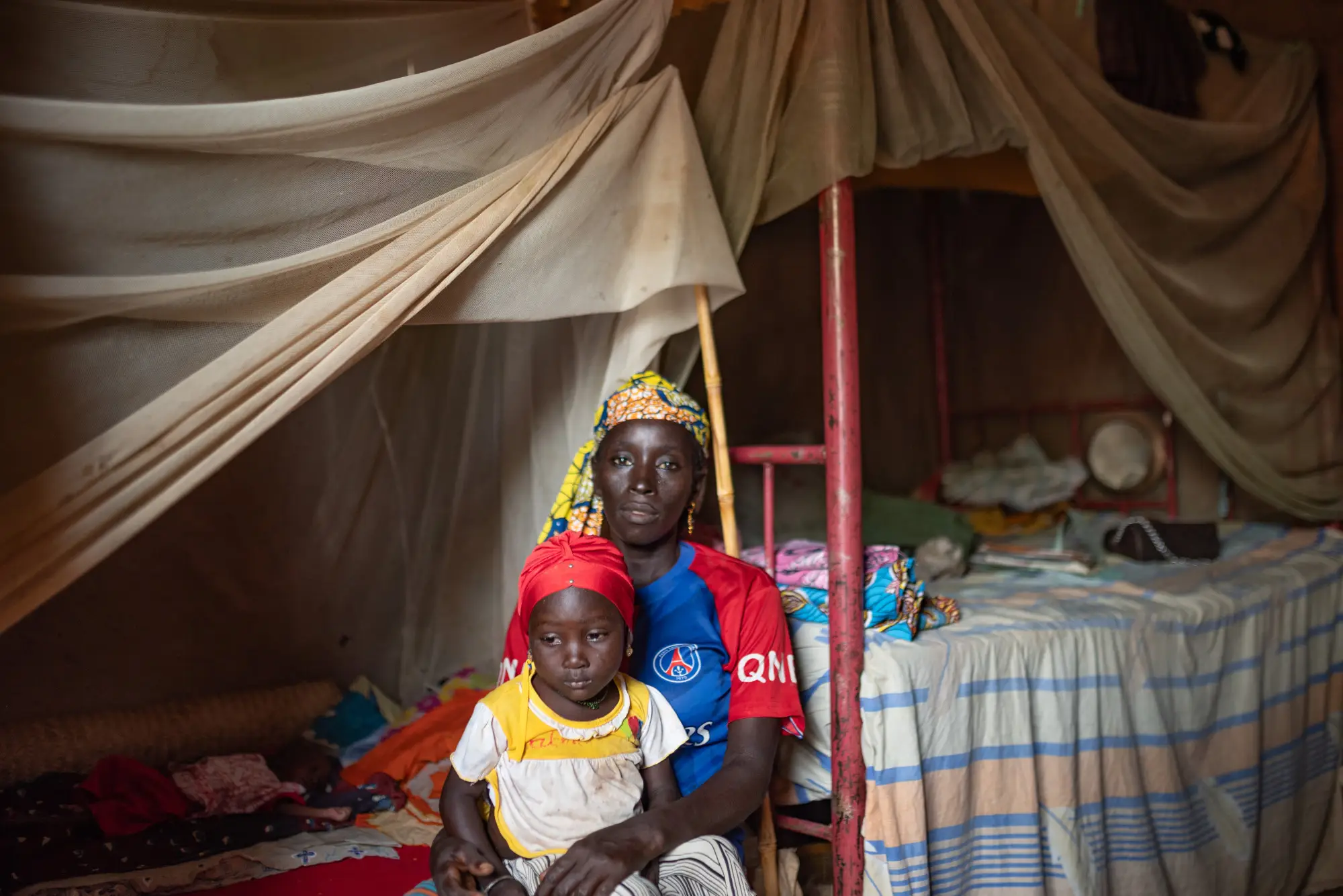 Caregiver and child on a bed with mosquito net, Nigeria
