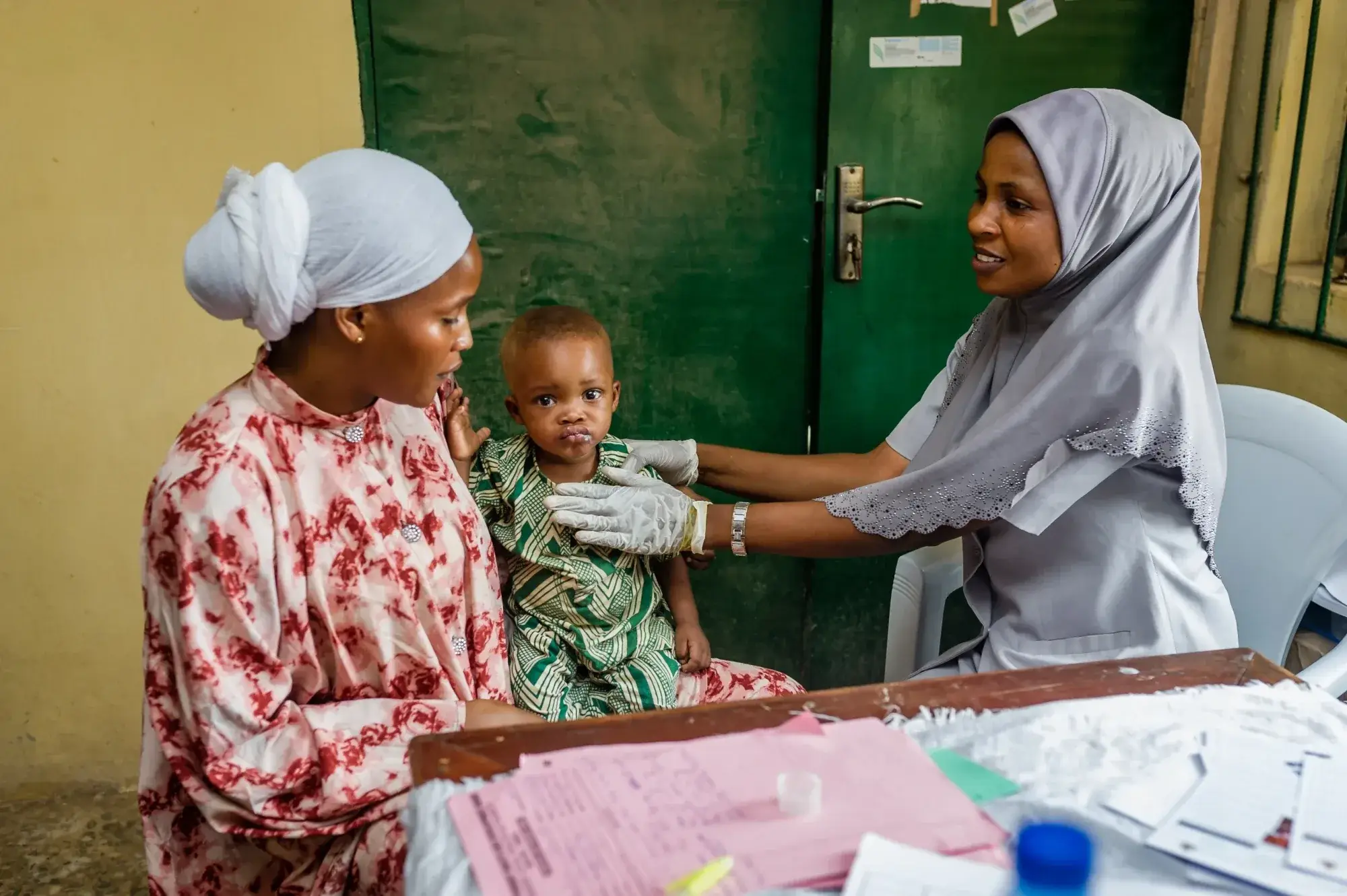 A child sitting on a woman's lap is assessed by a female healthcare worker