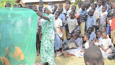 Community members, and in particular the young children, watch as the performers teach them how to hang a mosquito net before going to sleep.